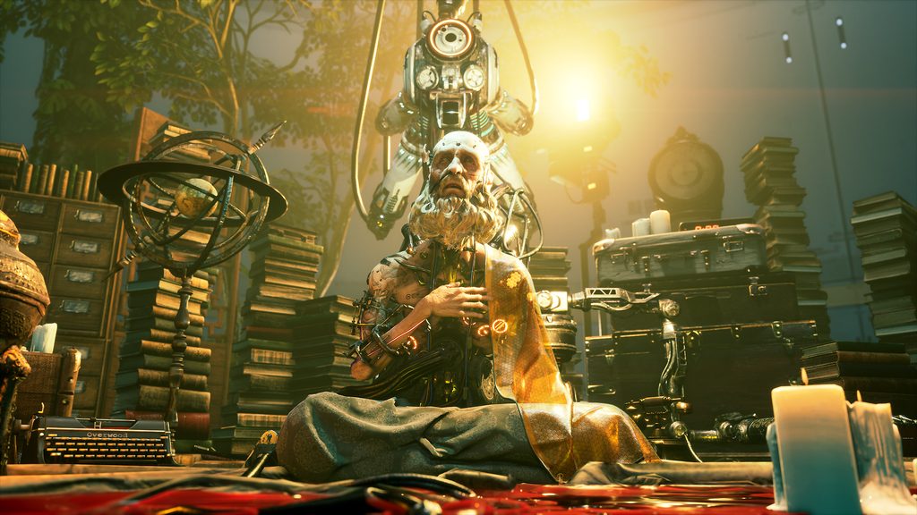 An elderly, heavily bearded figure, part humanoid, part cybernetic, sits amongst a collection of books and cases.